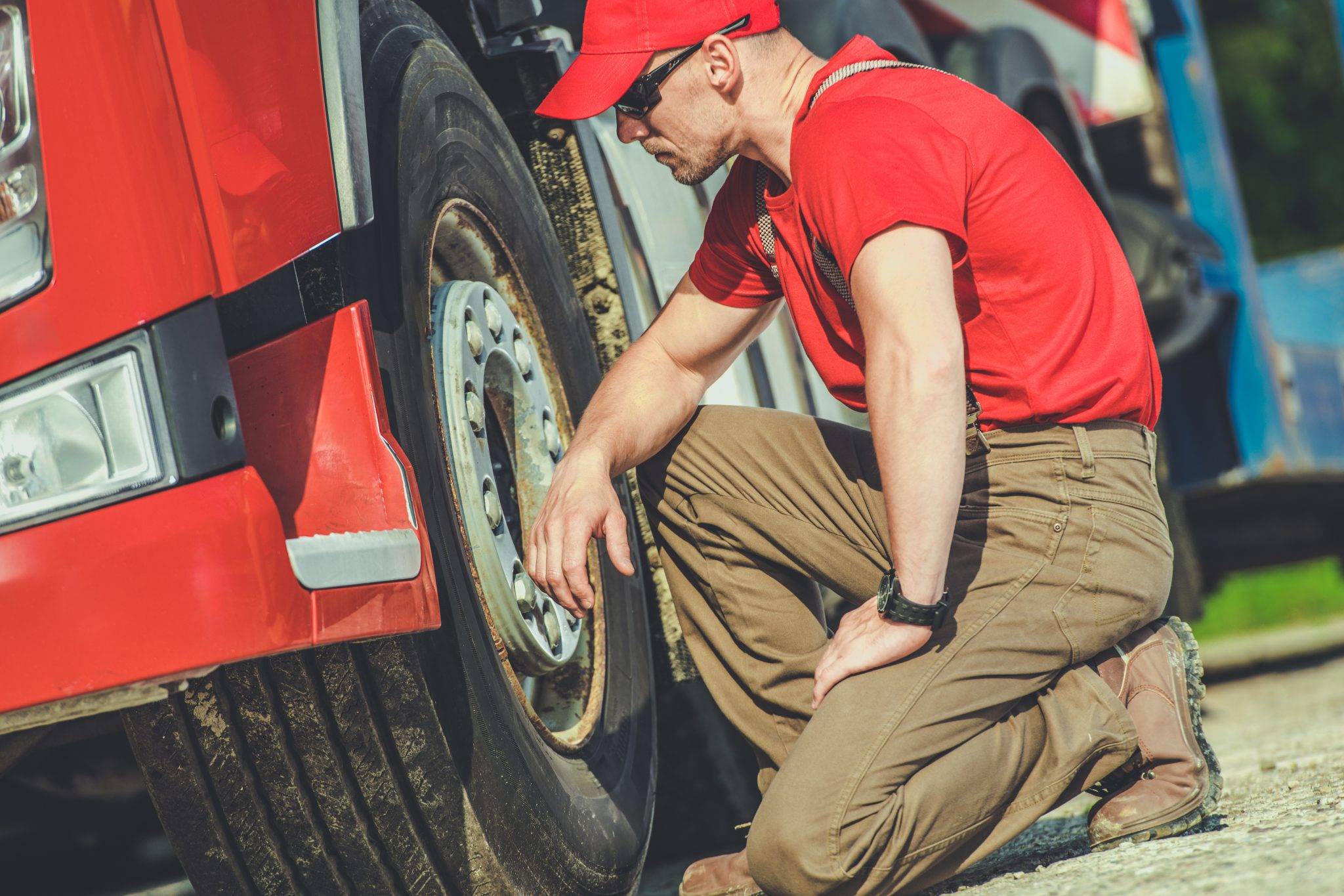 Truck Mechanic Inspecting Tire Of A Red Truck On A Sunny Day In A Service Area